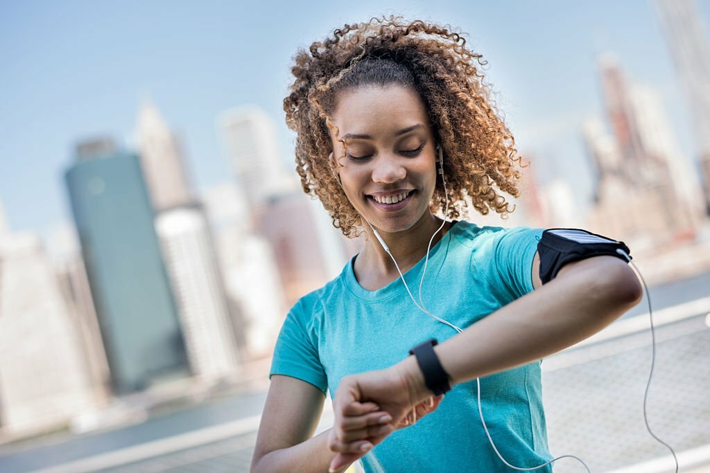 An active woman wearing an armband for her cellphone and tracking her workout progress with a smart watch