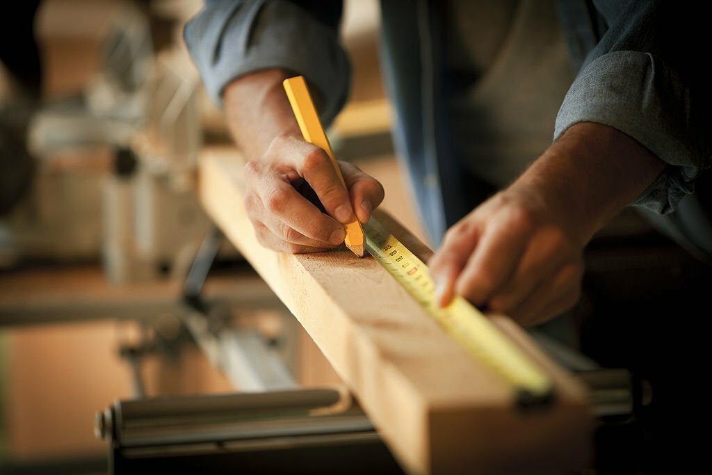 Closeup cropped view of a carpenter marking a measurement on a wooden plank. Horizontal shot.